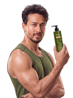 Tiger Shroff in an olive green tank top looking at the camera while holding a PROWL Daily Body Lotion bottle.