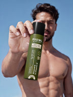 Tiger shroff holding a can of PROWL Body Hair Removal Spray against a bright blue sky background.