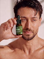 Shirtless Tiger Shroff holding a bottle of PROWL Brightening Face Serum close to his face.