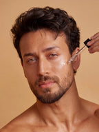 Shirtless Tiger Shroff using a dropper to apply PROWL Acne Control Face Serum to his cheek against a warm beige background.